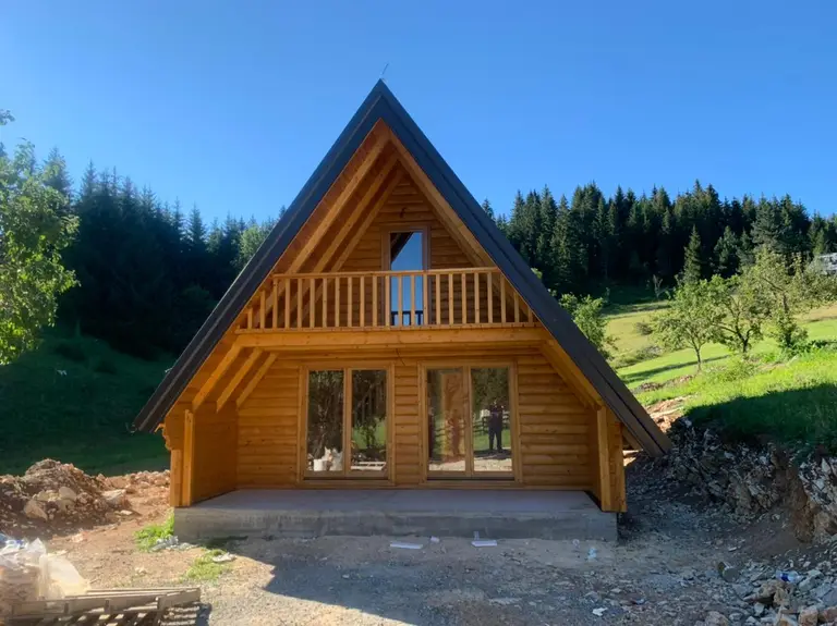 A-frame kuća od drveta sa balkonom na zabatu, ispod šume
