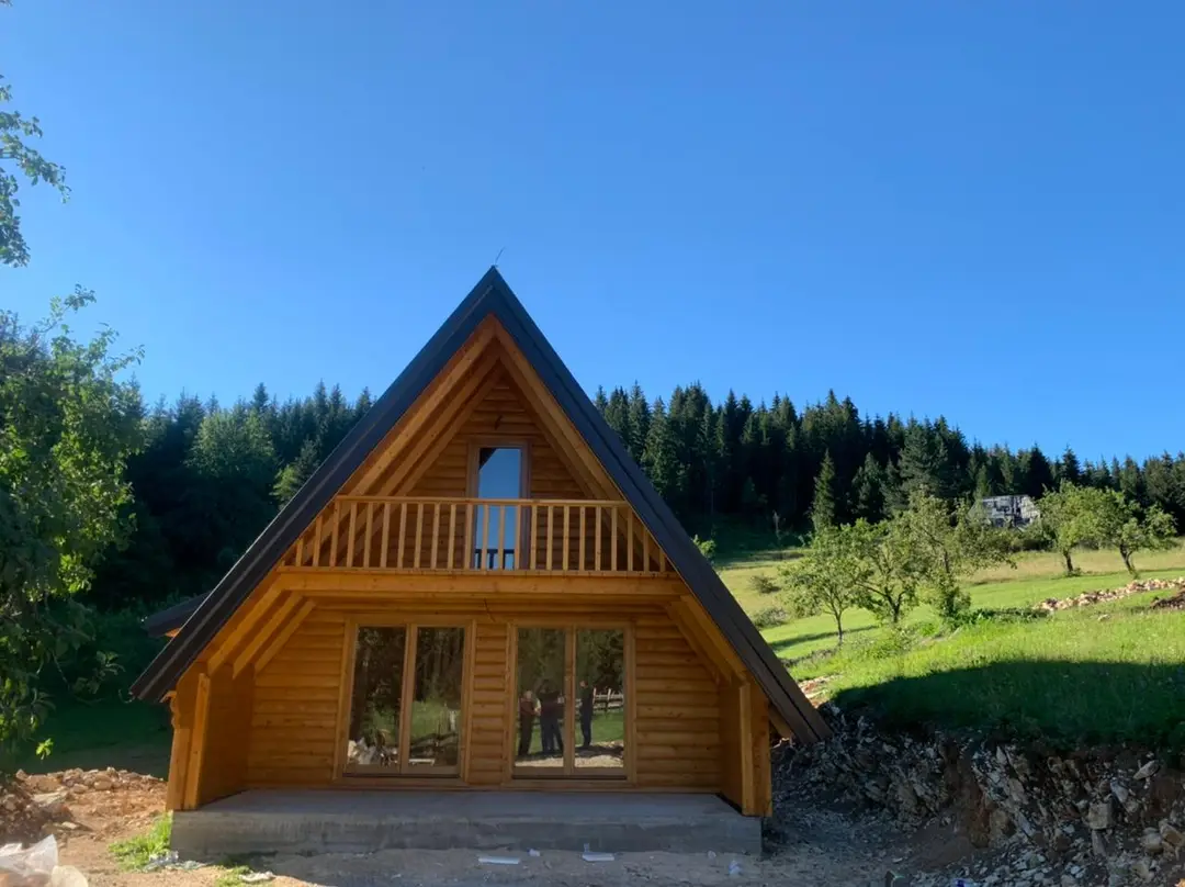 Završena A-frame kuća od drveta sa balkonom na livadi