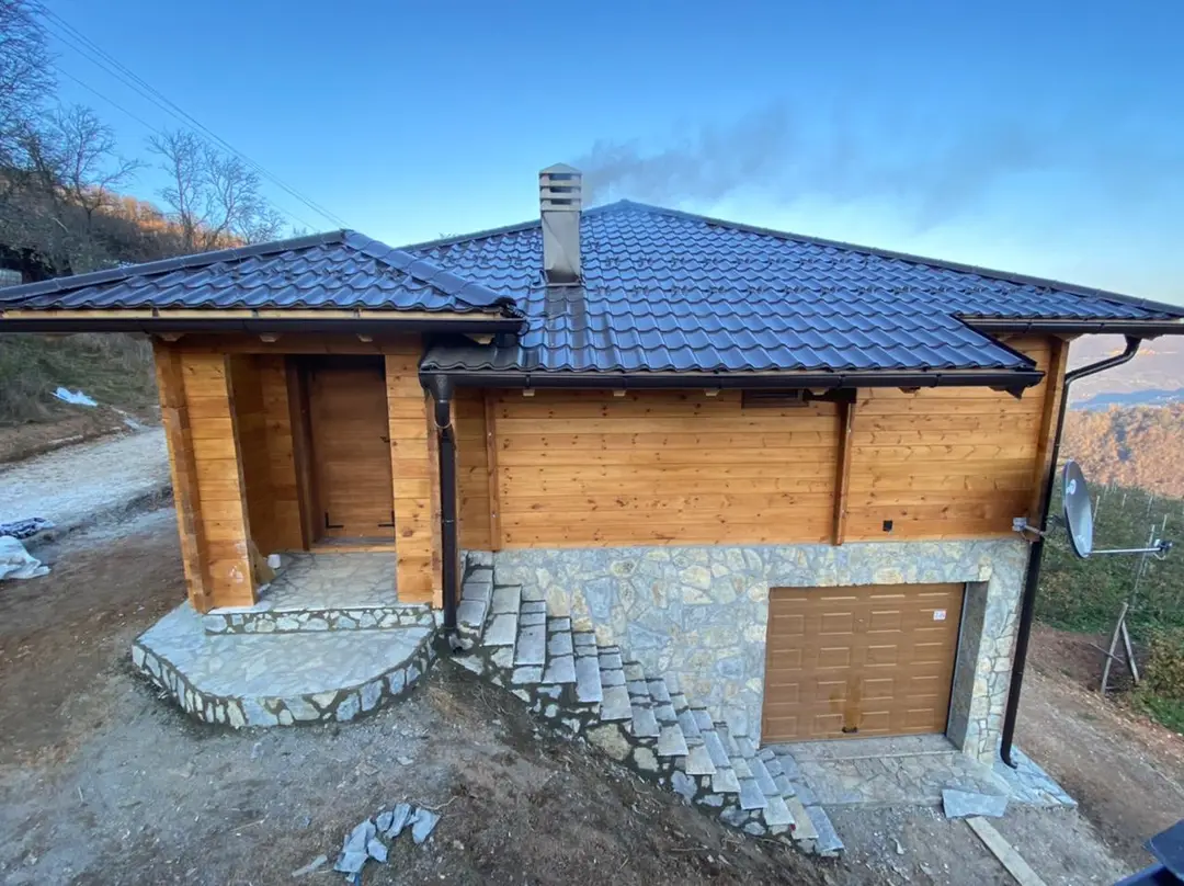 Log house with a blue roof and a garage in the stone ground floor