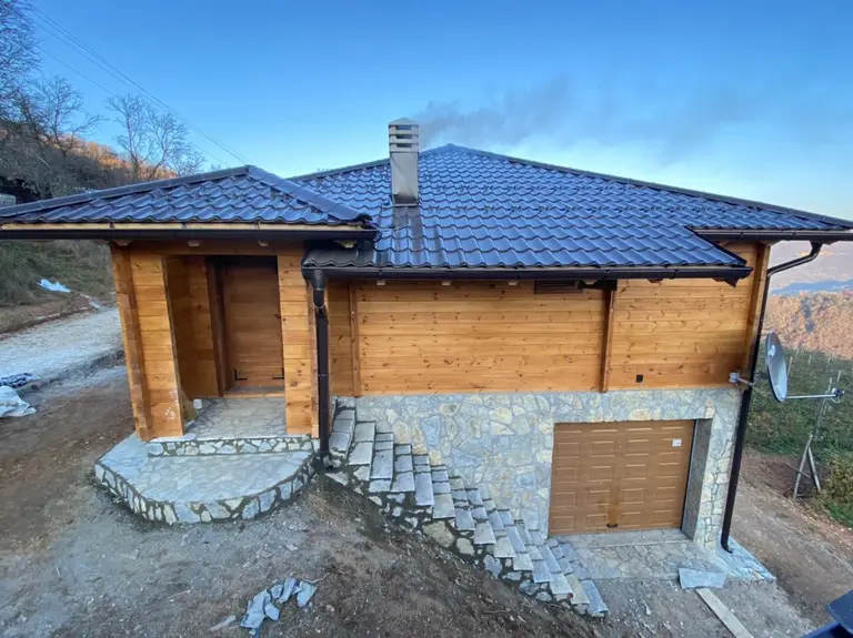 Log house with a blue roof and a garage in the stone ground floor
