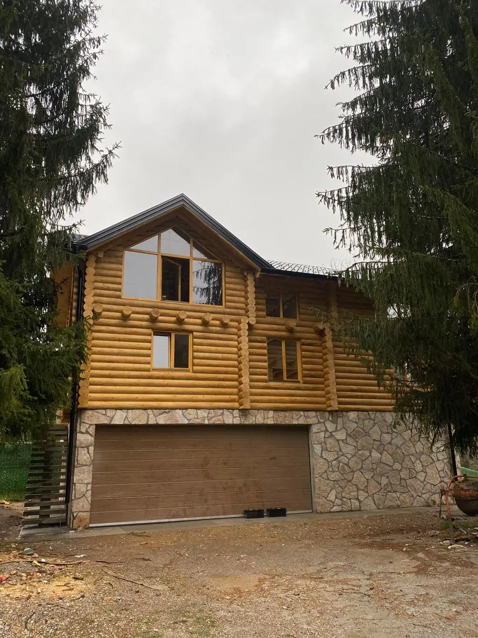 Two-storey log house with a garage in the stone base, surrounded by pines