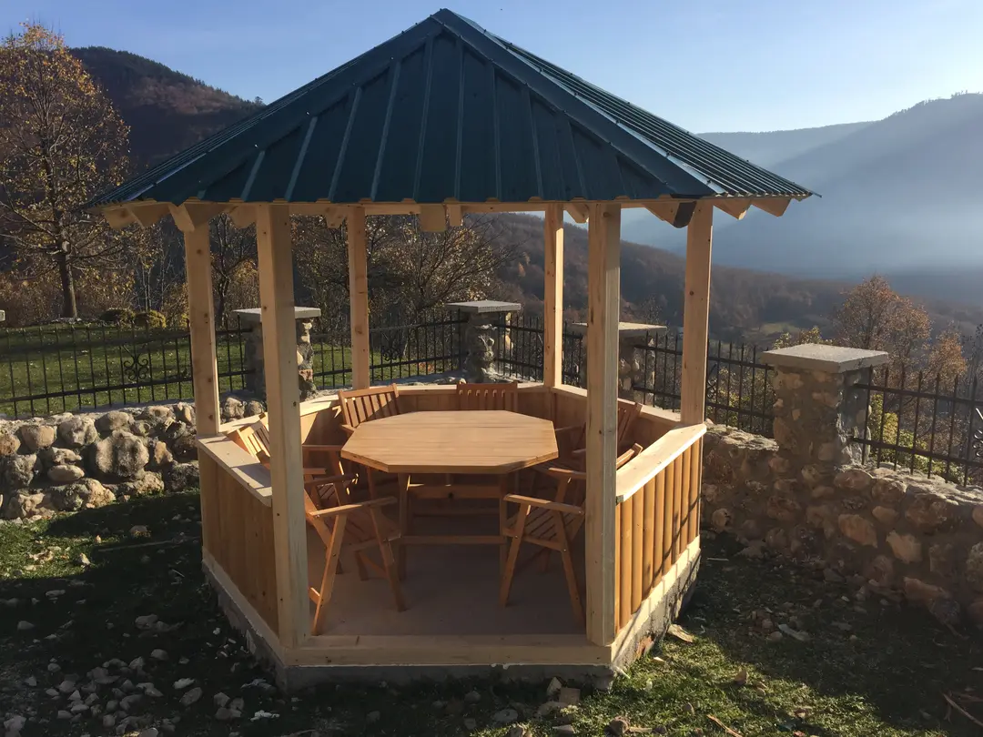 Wooden gazebo with a round table on a stone terrace above a valley