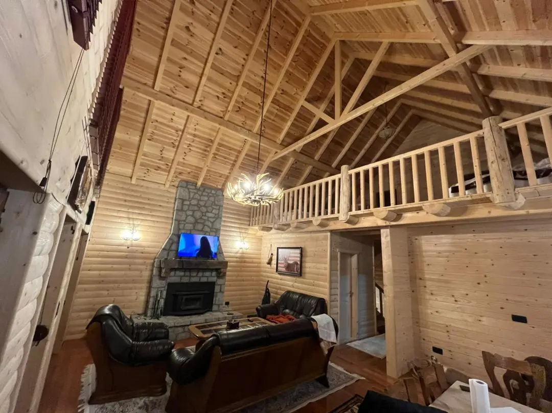 Log house interior with a gallery, stone fireplace and wooden ceiling