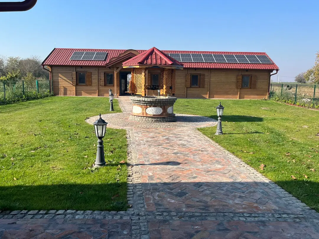 Single-storey log house with solar panels on the roof and a stone well in front
