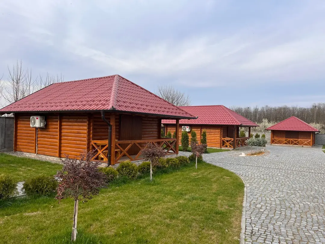 Log houses with red roofs and a gazebo at the end of a paved driveway