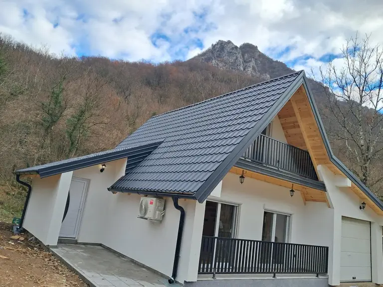 Montažna kuća sa bijelom fasadom, tamnim krovom i balkonom, bočni pogled