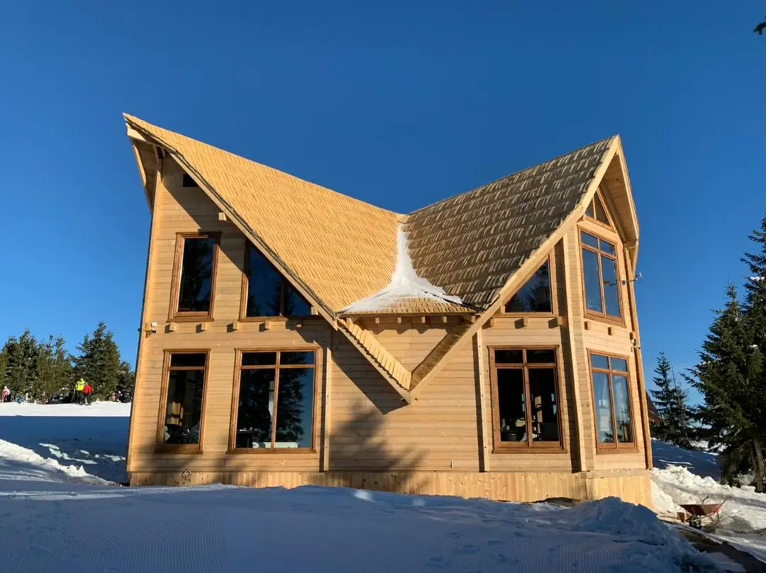 Wooden house with multiple gables and large windows in the snow