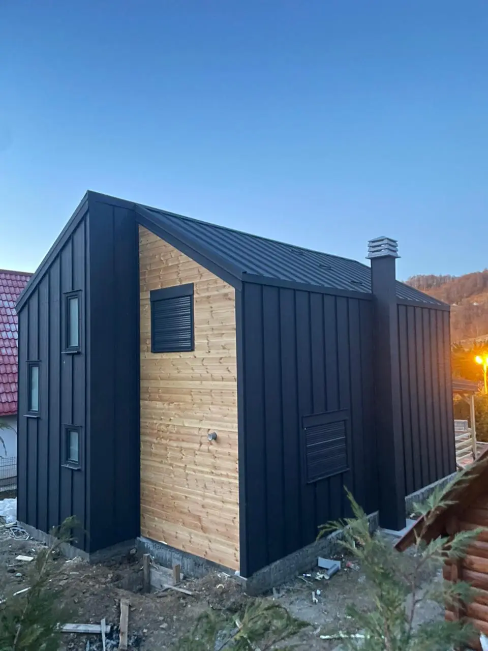 Corner of a modern house, black metal and light timber cladding at dusk