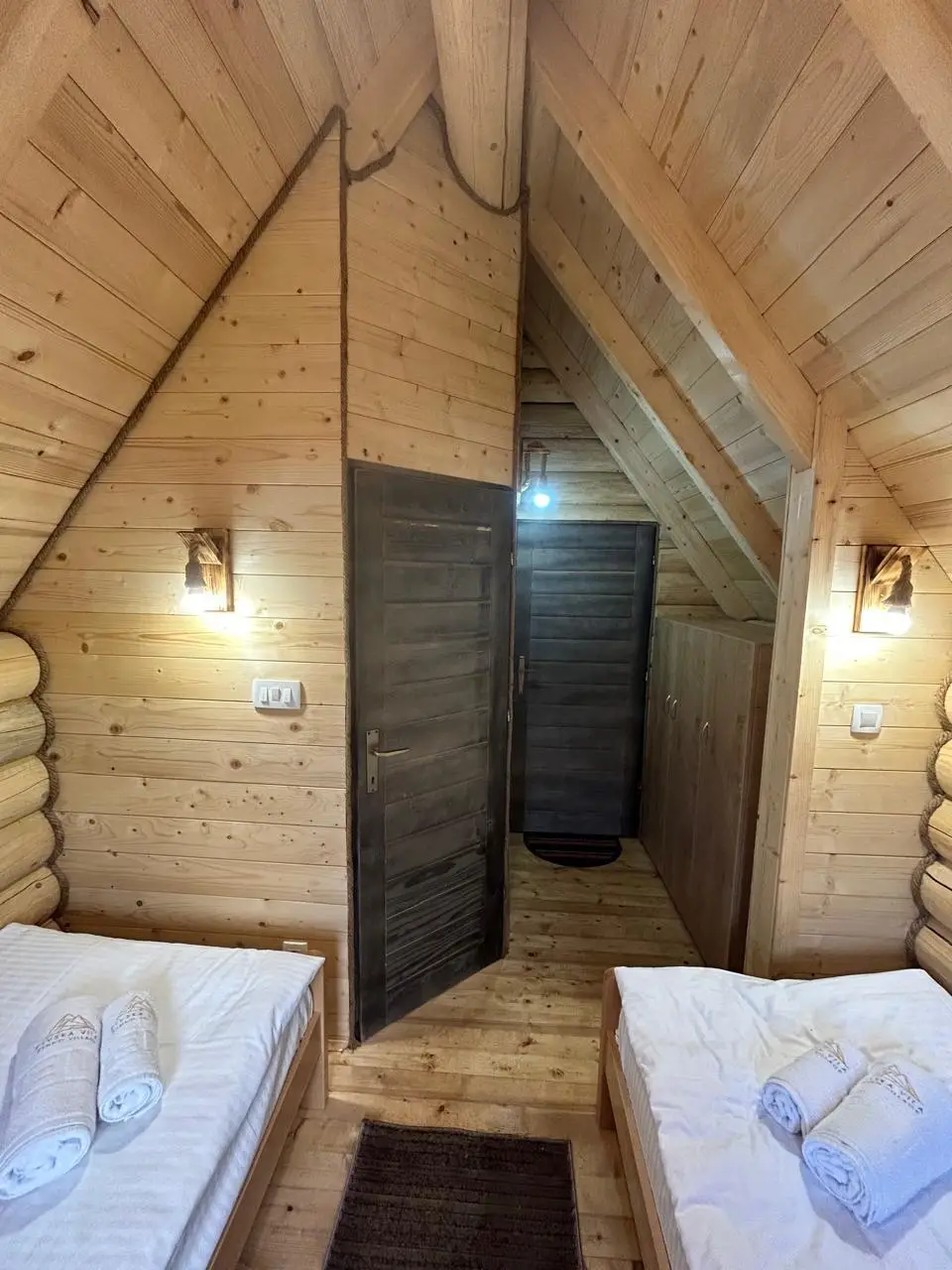 Attic of a log cabin with two beds and wall lights