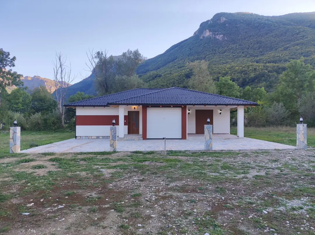 Single-storey prefab house with a garage and fence, below a mountain