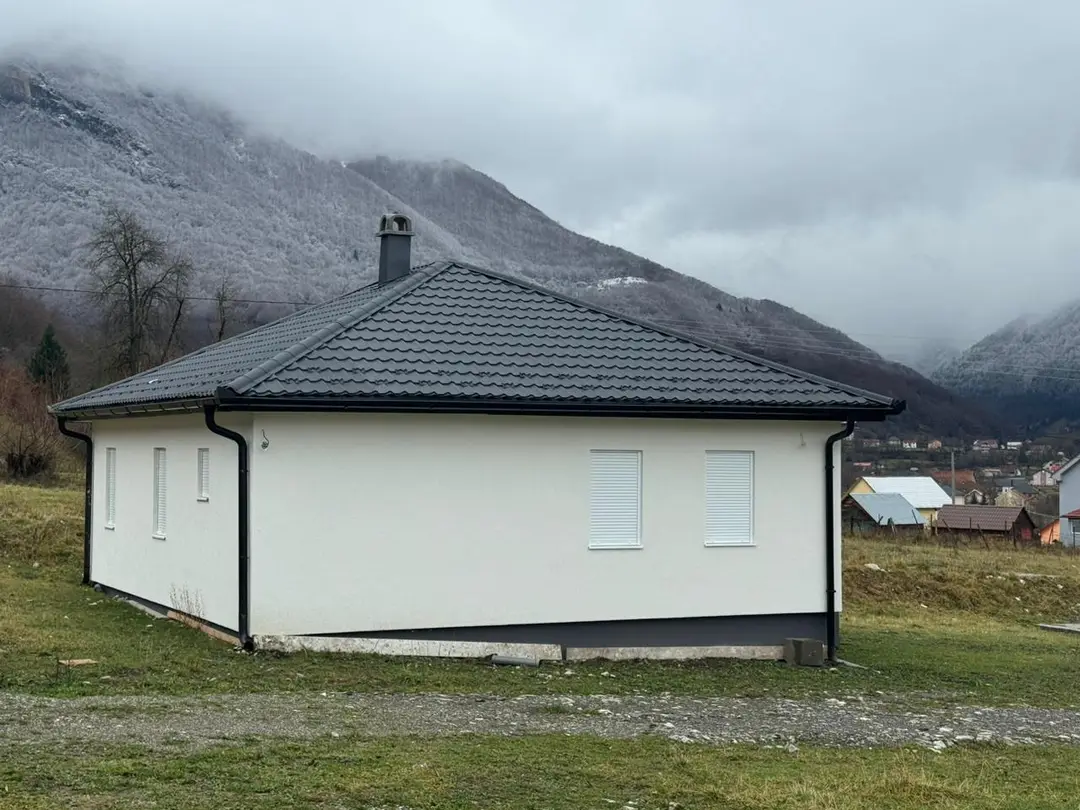 Single-storey house with a hipped roof and white facade under clouds
