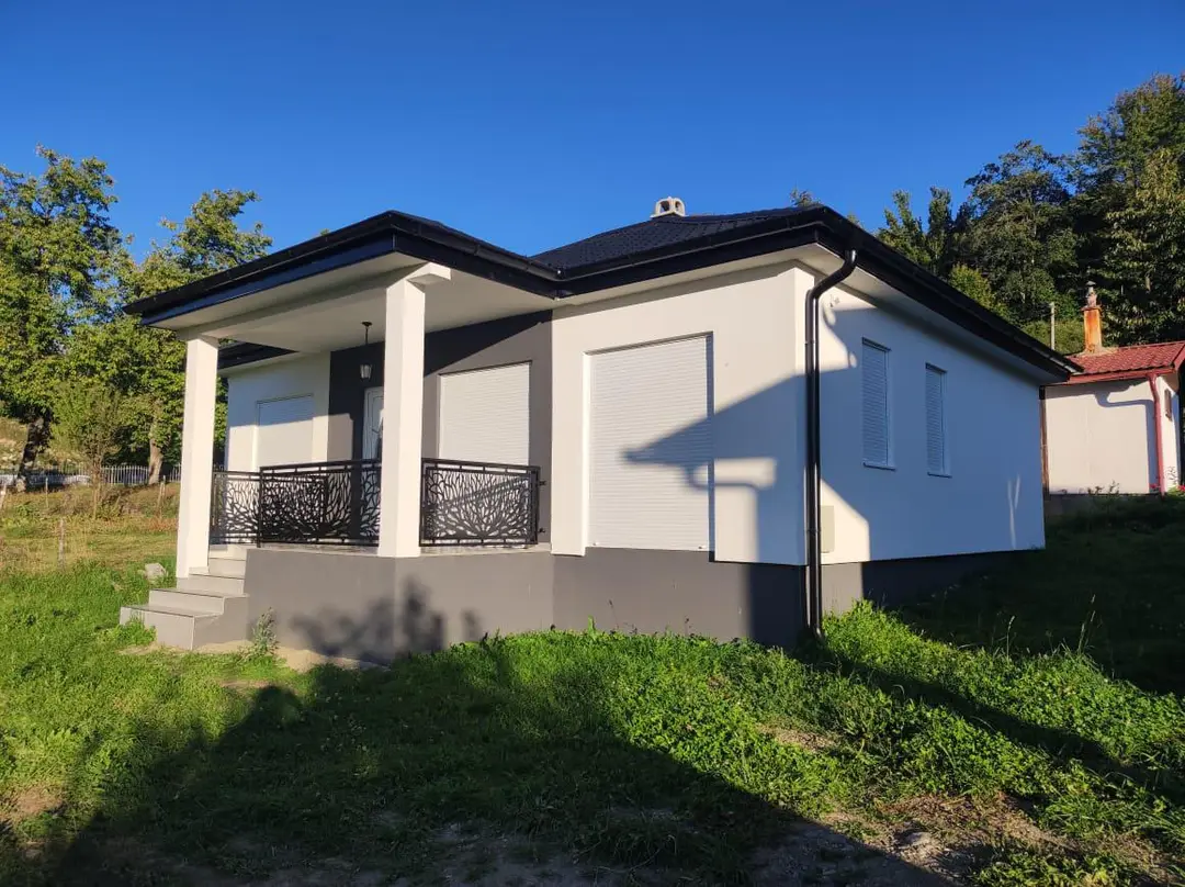 White single-storey house with a porch on a green plot, sunny day