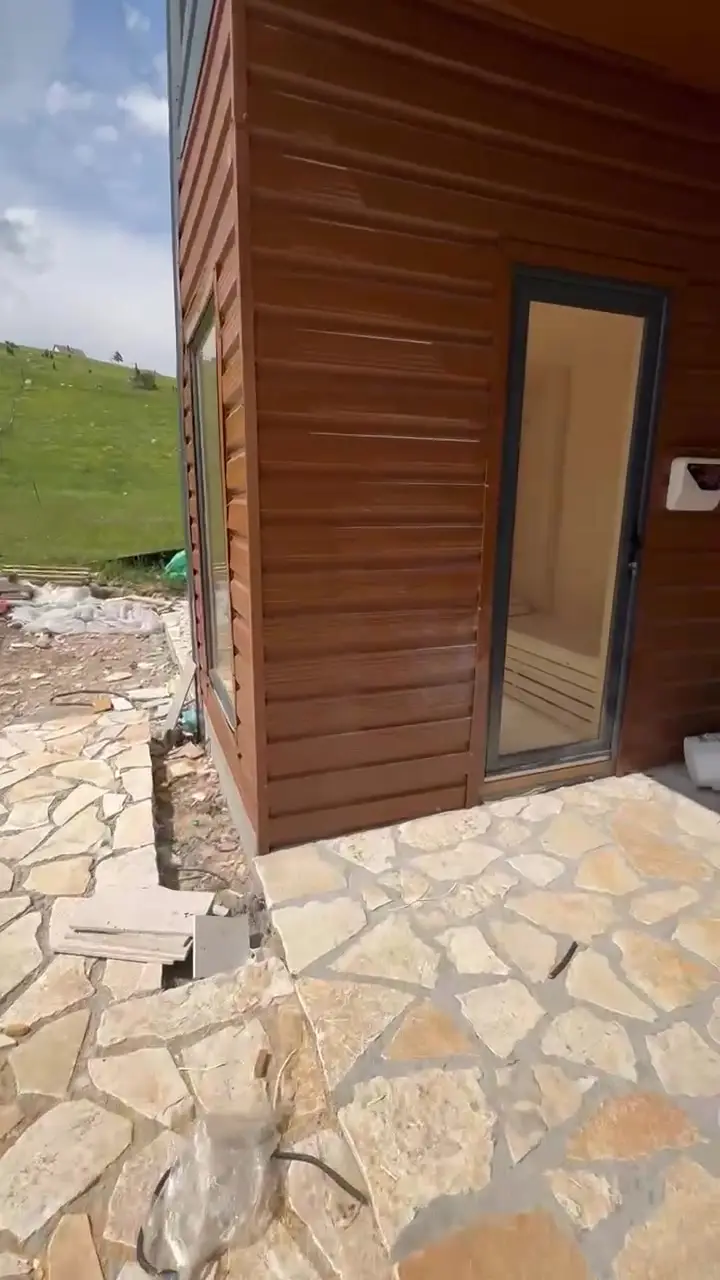 Drvena sauna u dvorištu sa staklenim vratima, pored kamene staze