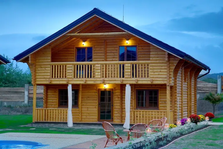 Two-storey log house with a balcony and lights on at dusk